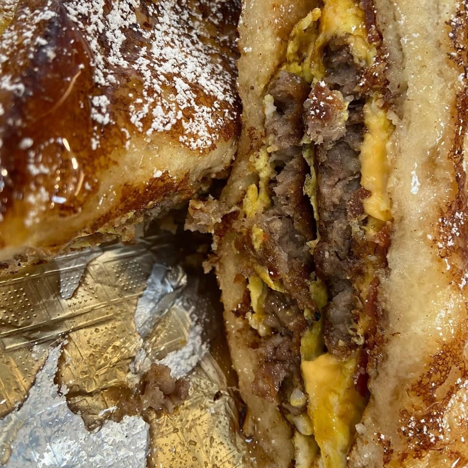 Close-up of a French toast sandwich with sausage, egg, and cheese, dusted with powdered sugar.