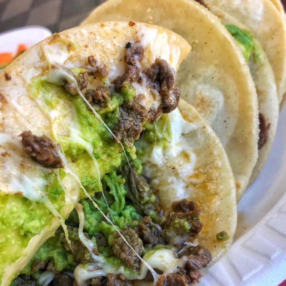 Close-up of three Vaqueros Over the Fire tacos with melted cheese, ground beef, and guacamole.