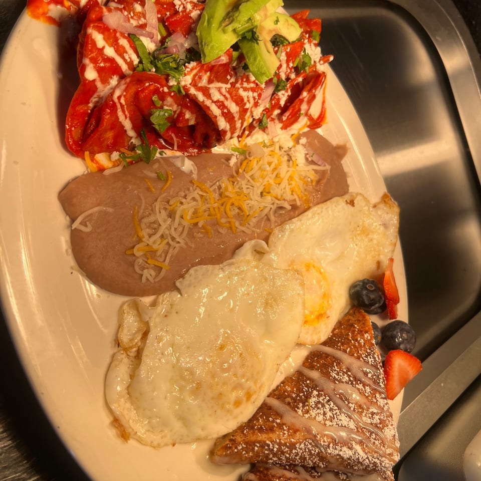 A Mexican breakfast plate with chilaquiles, refried beans, fried eggs, and French toast with berries.