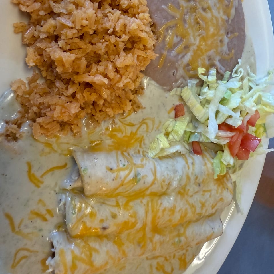 Three enchiladas covered in white sauce and shredded cheese, with rice, refried beans, and salad.
