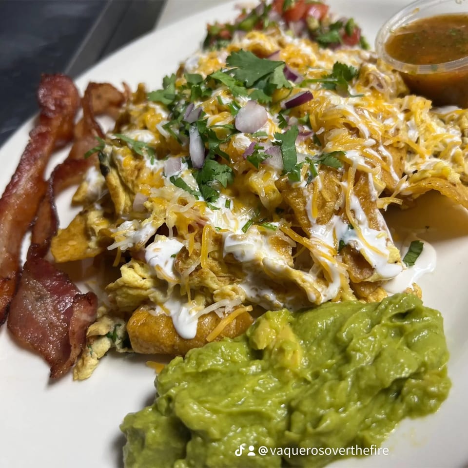Mexican breakfast plate with chilaquiles, scrambled eggs, bacon, guacamole, salsa, and pico de gallo.