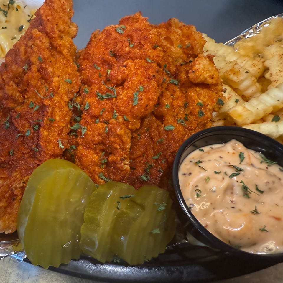Spicy fried chicken tenders with waffle fries, pickles, and a side of creamy sauce.