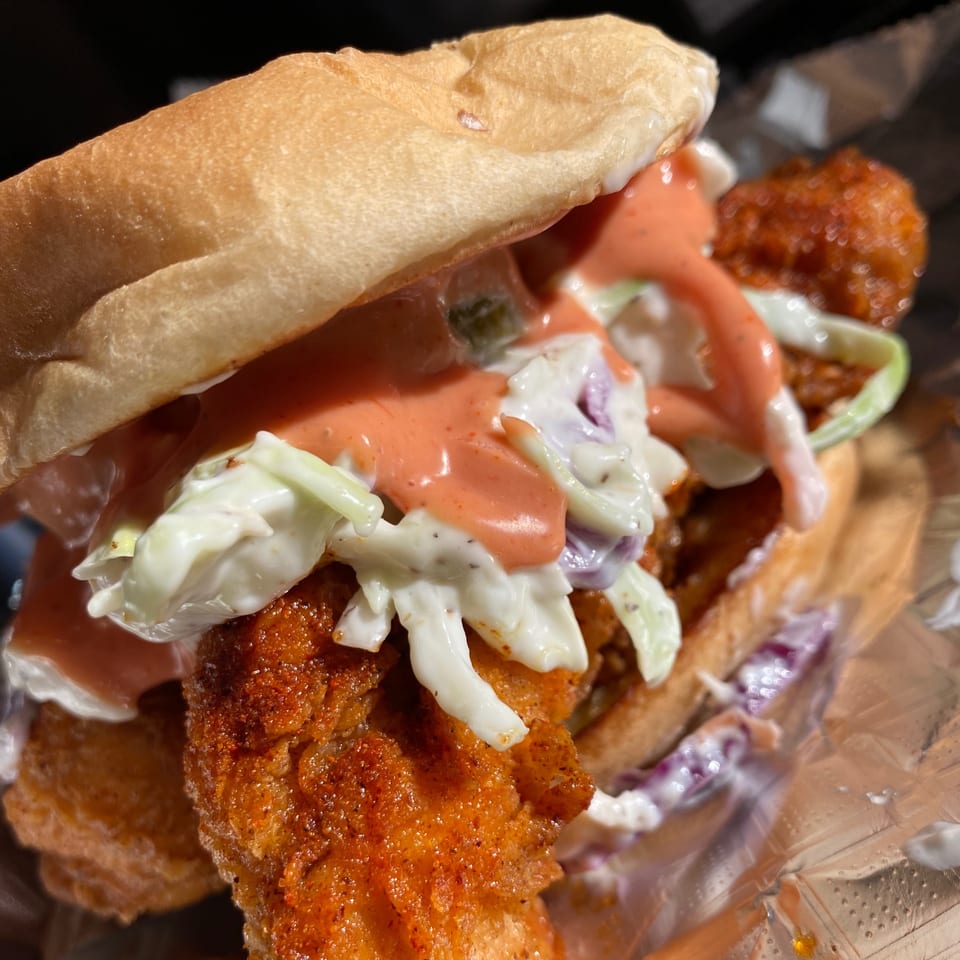 Close-up of a Vaqueros fried chicken sandwich with coleslaw and orange sauce on a bun.