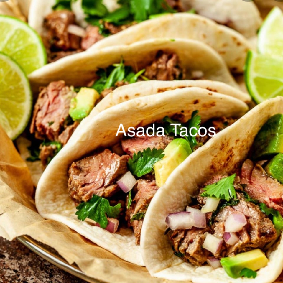 Close-up of three Vaqueros Over the Fire asada tacos with meat, cilantro, onions, and avocado.