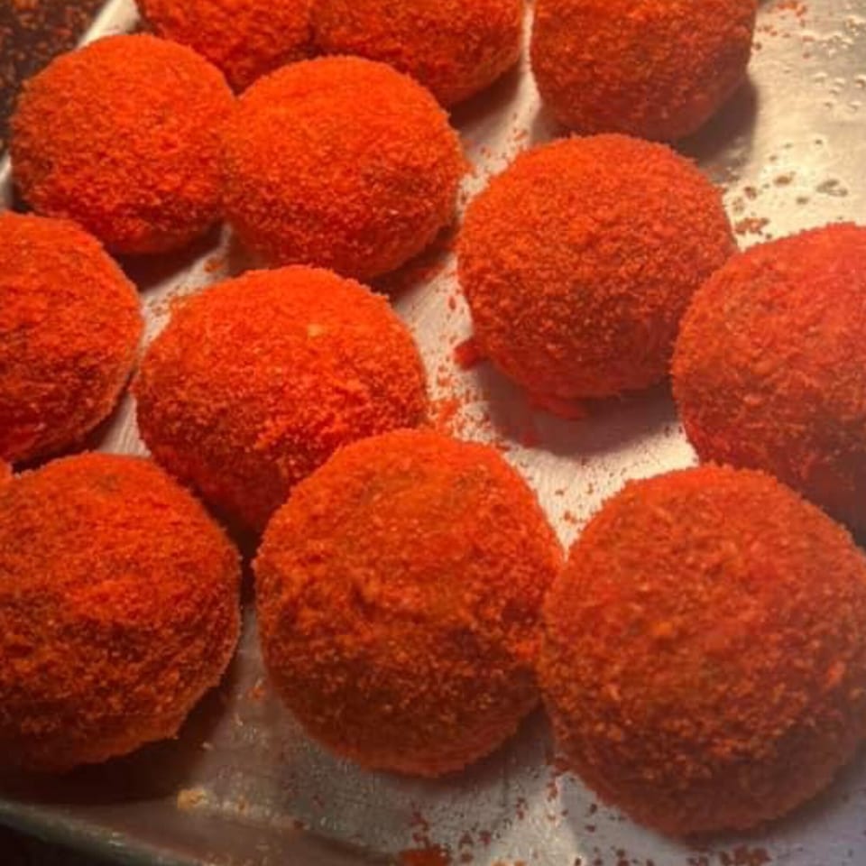A tray of round, bright red, breaded Mexican appetizers, possibly Vaqueros Over the Fire's signature dish.