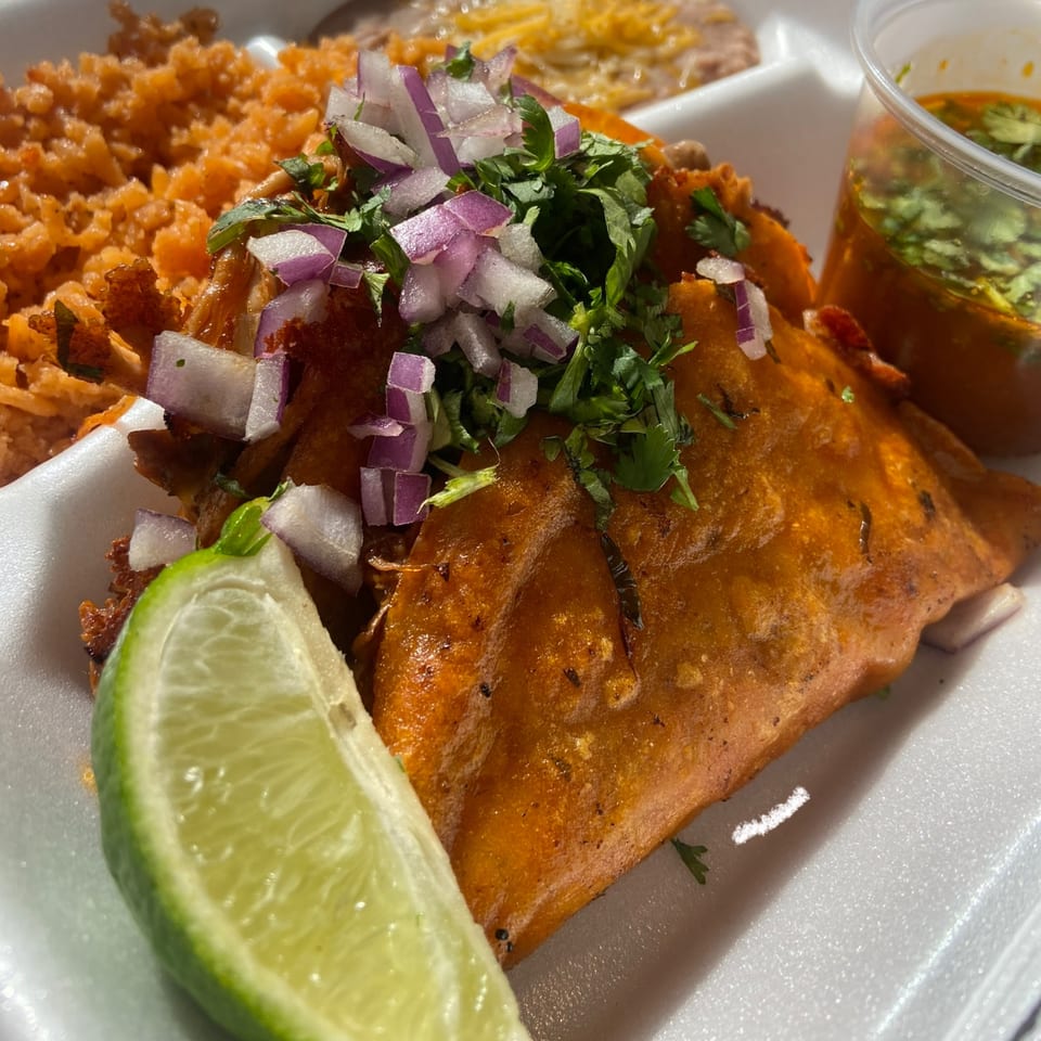 Vaqueros Over the Fire birria taco with rice, beans, lime, and a side of consommé.