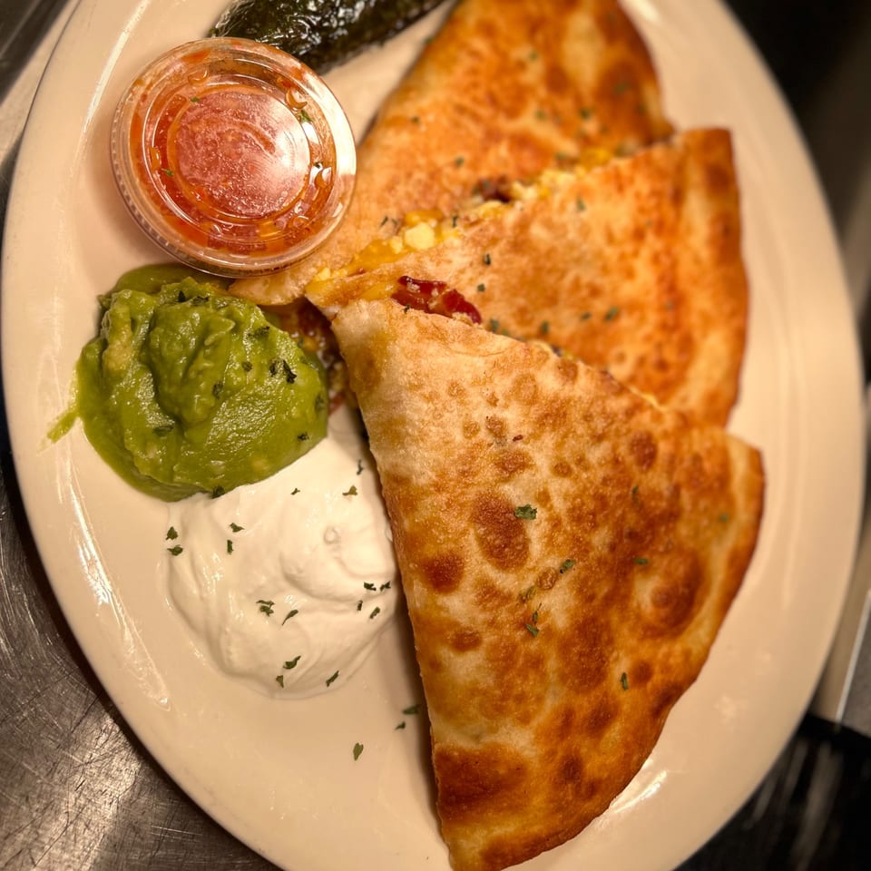 Golden-brown quesadillas with guacamole, sour cream, and salsa on a white plate.