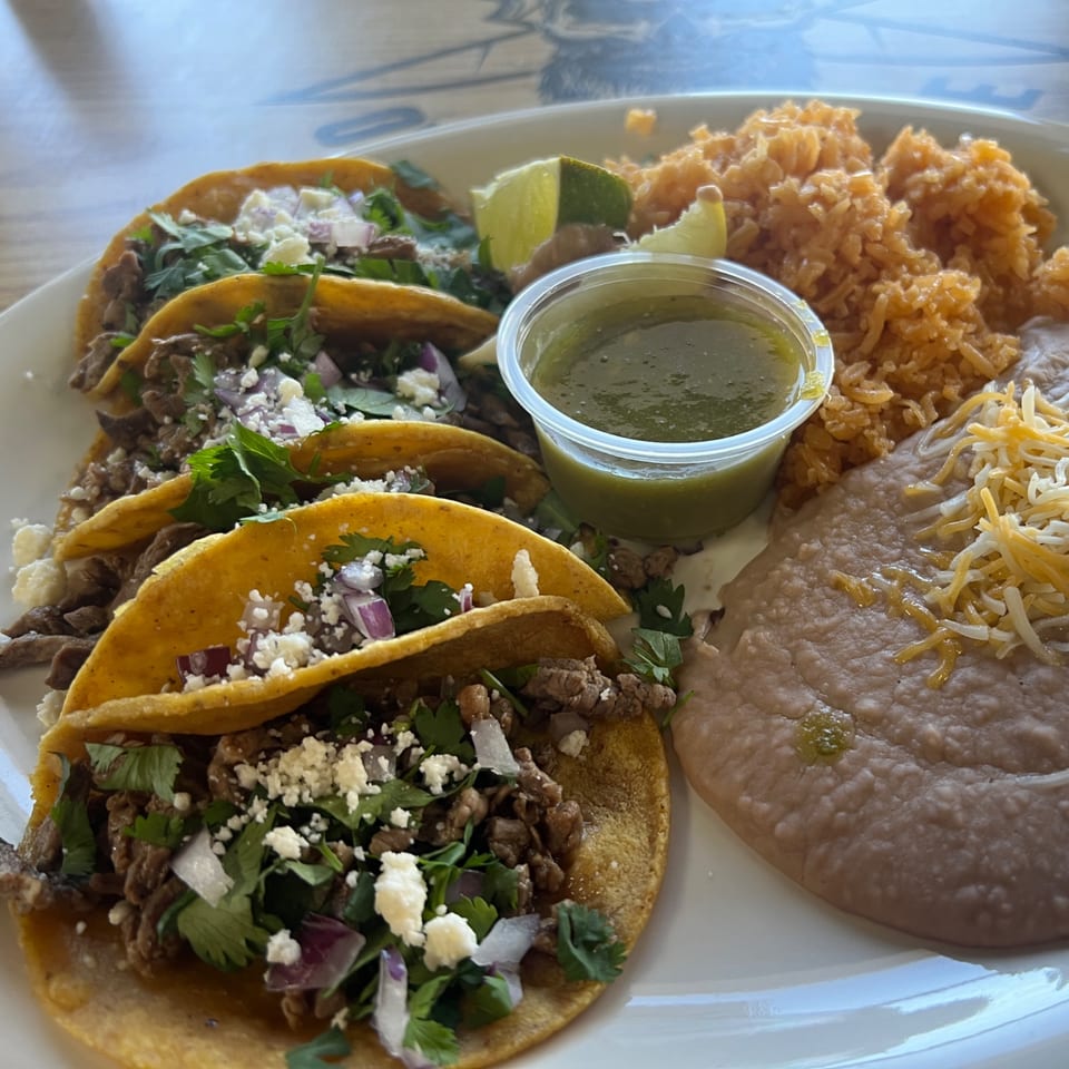 Four carne asada street tacos with cilantro, onions, and cotija cheese, served with rice and refried beans.
