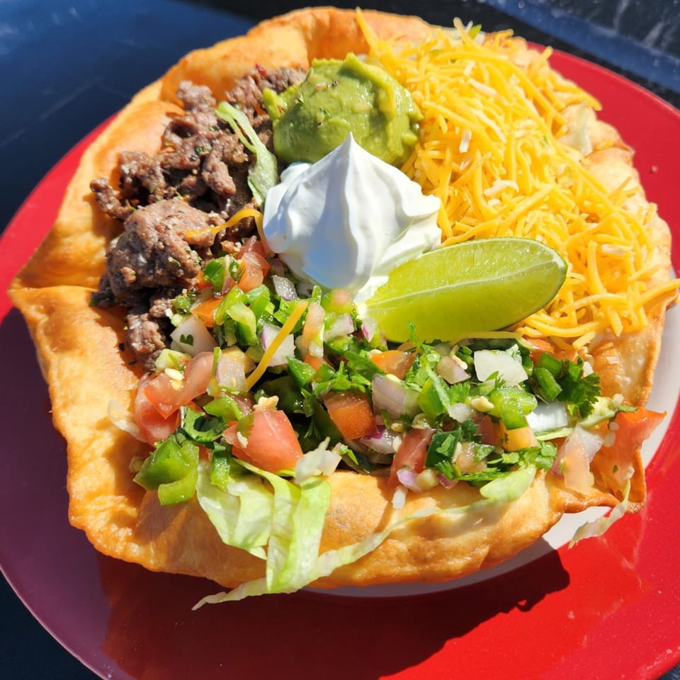 A Vaqueros Over the Fire taco salad in a fried tortilla bowl with beef, cheese, guacamole, sour cream, and pico de gallo.