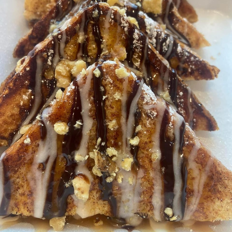 Mexican dessert with fried pastry triangles drizzled with chocolate, white icing, and chopped nuts.