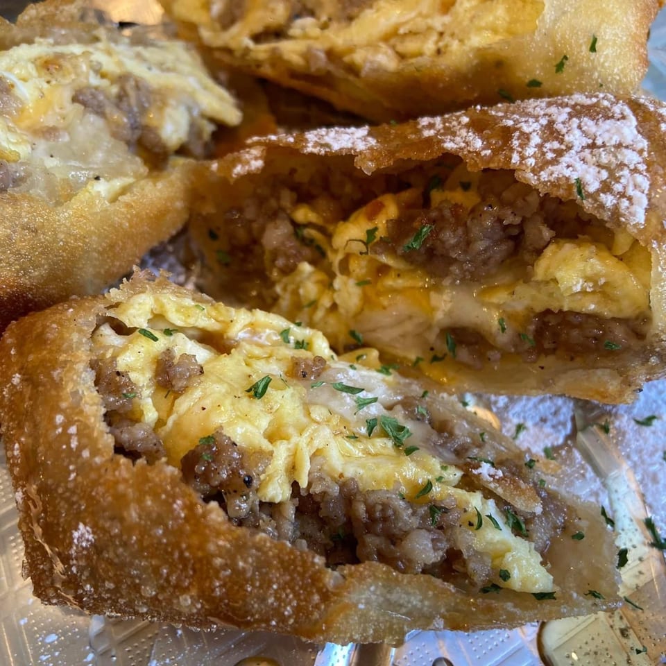 Close-up of a deep-fried Mexican pastry, cut open to reveal a filling of scrambled eggs and ground meat.
